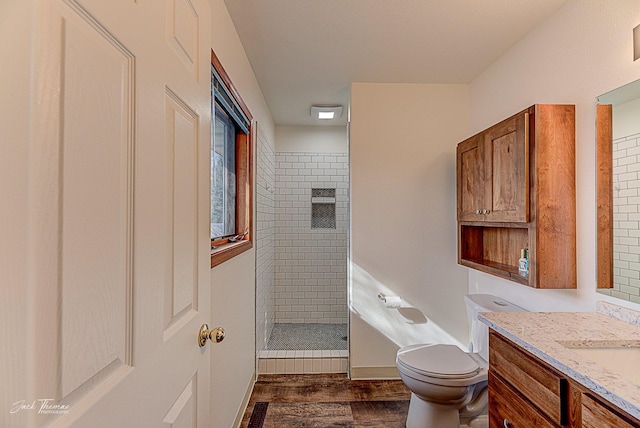 full bathroom with visible vents, toilet, a tile shower, vanity, and wood finished floors