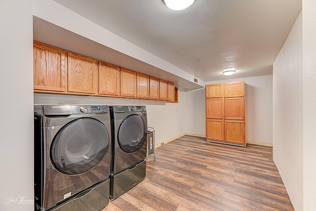 clothes washing area featuring cabinet space, washing machine and dryer, baseboards, and wood finished floors