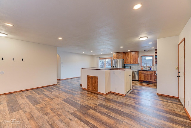 kitchen featuring arched walkways, dark wood-style flooring, appliances with stainless steel finishes, brown cabinetry, and dark countertops