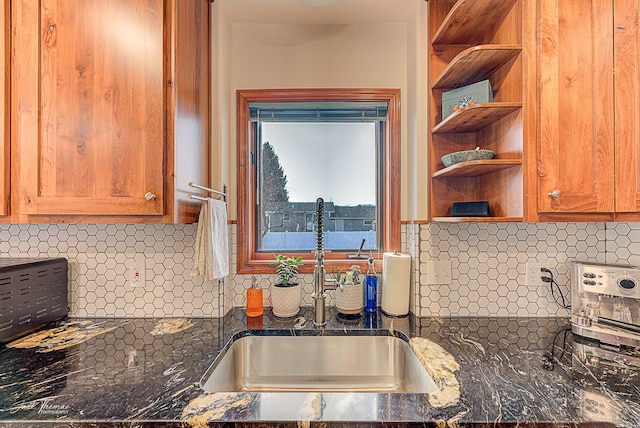 kitchen with open shelves, decorative backsplash, brown cabinetry, a sink, and dark stone counters