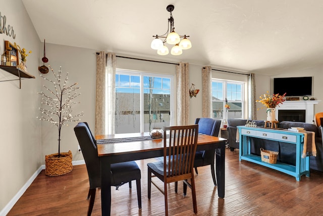 dining area with lofted ceiling, a chandelier, a fireplace, wood finished floors, and baseboards