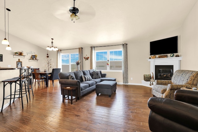 living area featuring lofted ceiling, dark wood-type flooring, a glass covered fireplace, ceiling fan, and baseboards