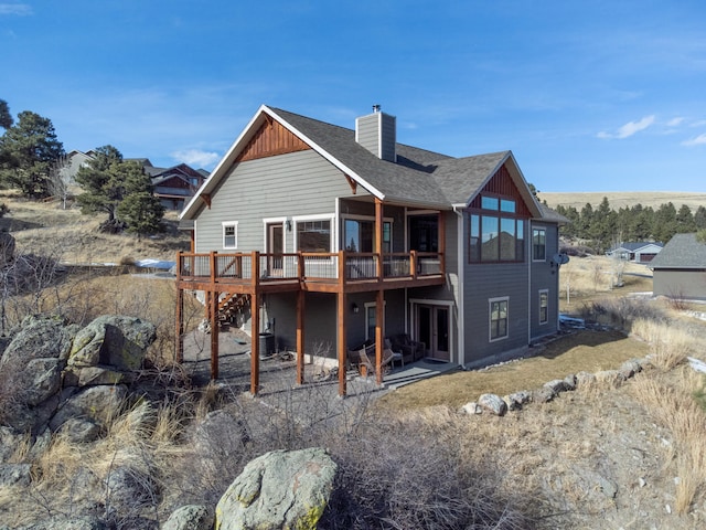 back of property with a shingled roof, a chimney, and a deck