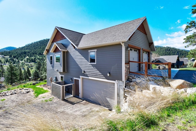 view of side of home featuring roof with shingles, a mountain view, a garage, stone siding, and driveway