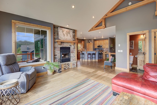 living area featuring recessed lighting, light wood-style flooring, a stone fireplace, high vaulted ceiling, and baseboards