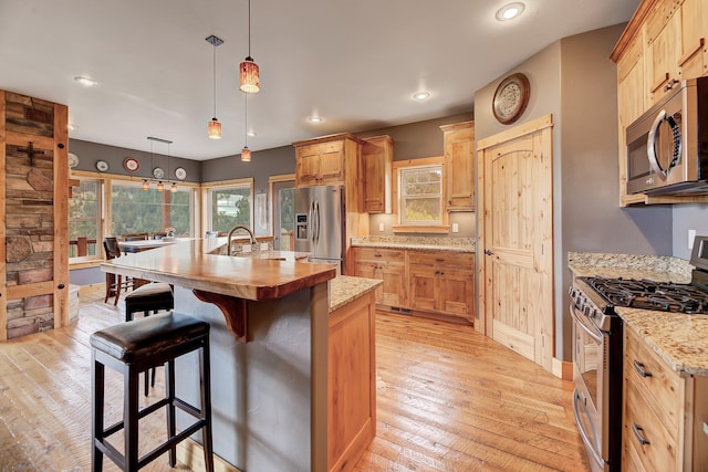 kitchen with a center island with sink, stainless steel appliances, light wood-style flooring, a sink, and a kitchen breakfast bar