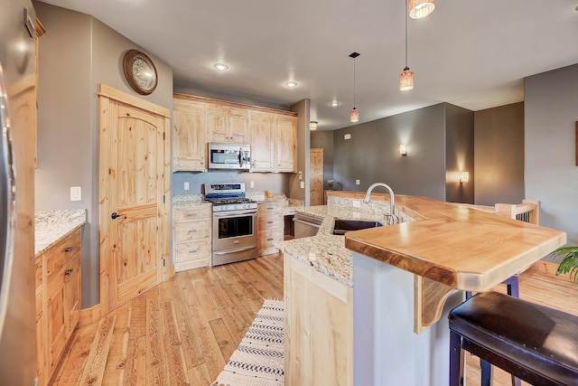 kitchen featuring a breakfast bar, decorative light fixtures, light wood-style flooring, appliances with stainless steel finishes, and a sink