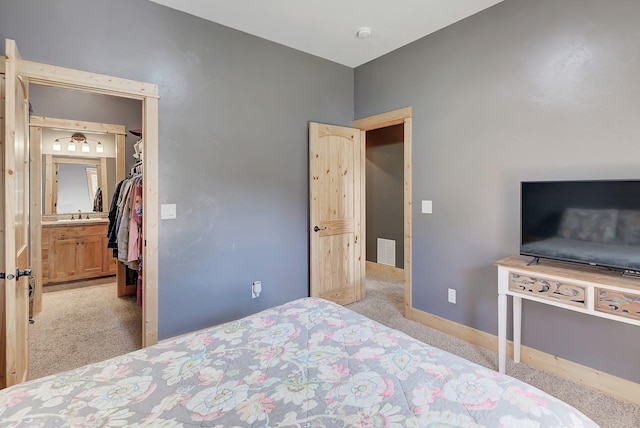 bedroom featuring baseboards, visible vents, light colored carpet, a walk in closet, and a sink