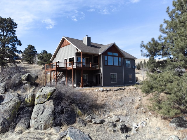 back of house with a chimney, stairway, a deck, and roof with shingles