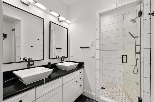 full bath with double vanity, a shower stall, baseboards, and a sink