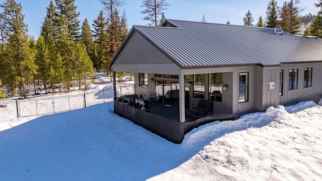 snow covered property featuring metal roof, board and batten siding, a standing seam roof, and fence