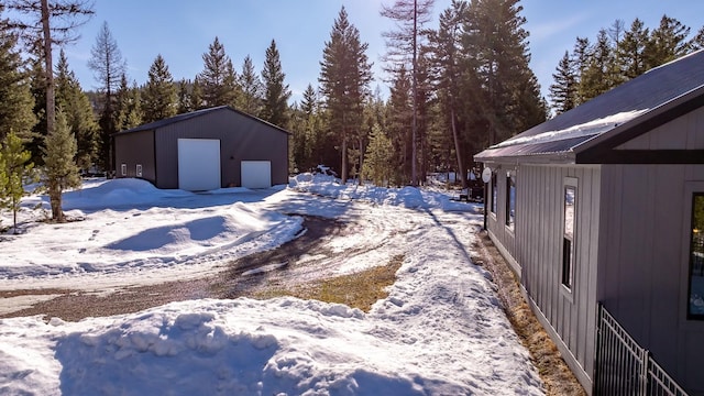 snowy yard featuring a garage, a forest view, and an outdoor structure