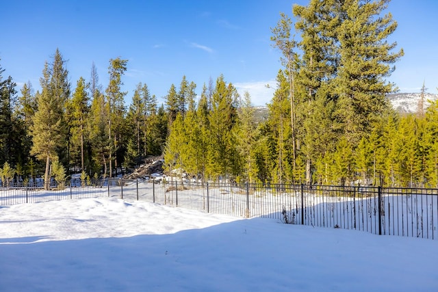 snowy yard featuring a forest view and fence