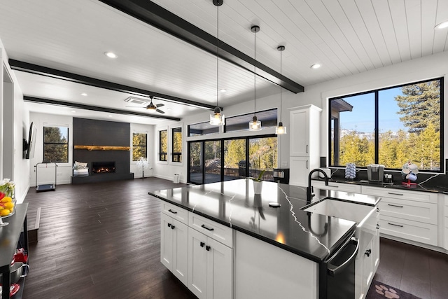 kitchen featuring a center island with sink, dark countertops, open floor plan, beamed ceiling, and a lit fireplace