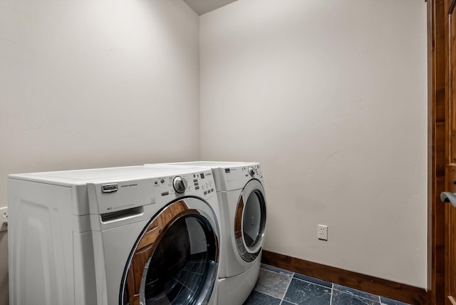 laundry area with laundry area, stone finish flooring, washer and clothes dryer, and baseboards