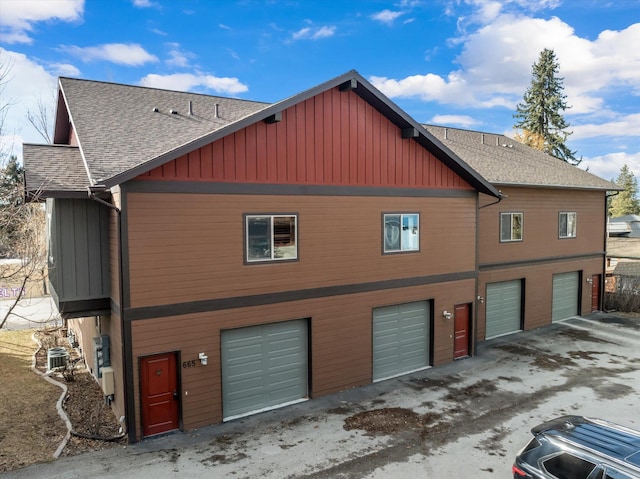 view of property exterior with a garage, roof with shingles, board and batten siding, and central AC unit