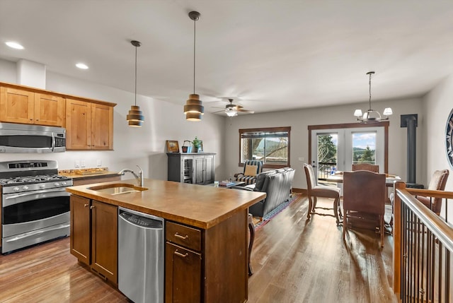 kitchen with pendant lighting, a center island with sink, appliances with stainless steel finishes, a sink, and wood finished floors