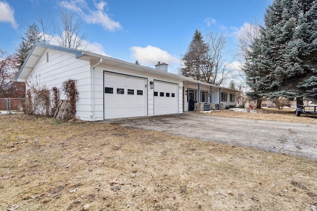 exterior space featuring aphalt driveway, a chimney, covered porch, an attached garage, and fence