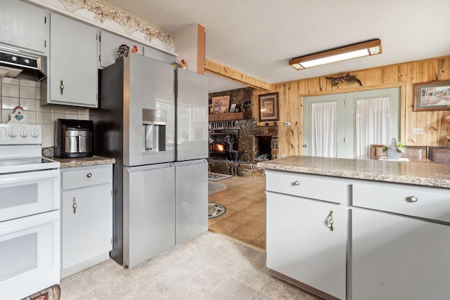 kitchen with wood walls, a wood stove, under cabinet range hood, stainless steel fridge, and double oven range
