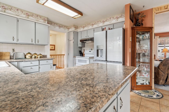 kitchen featuring a peninsula, white appliances, tasteful backsplash, light tile patterned flooring, and under cabinet range hood