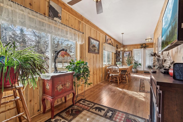 dining area with ceiling fan, wooden walls, and wood-type flooring