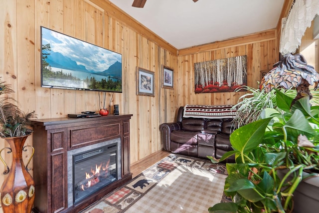 sitting room featuring a ceiling fan, wood walls, a glass covered fireplace, and wood finished floors