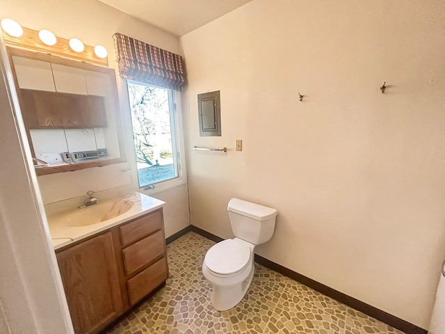 bathroom featuring electric panel, vanity, toilet, and baseboards