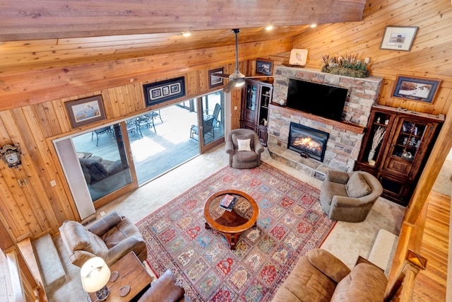 living room with a ceiling fan, vaulted ceiling with beams, wooden walls, carpet floors, and a fireplace