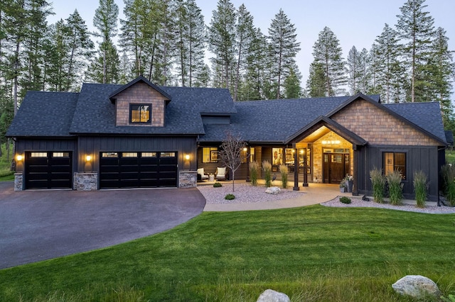 modern inspired farmhouse with aphalt driveway, roof with shingles, board and batten siding, a front yard, and a garage