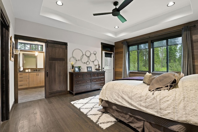 bedroom featuring recessed lighting, a raised ceiling, a barn door, dark wood-type flooring, and ensuite bath