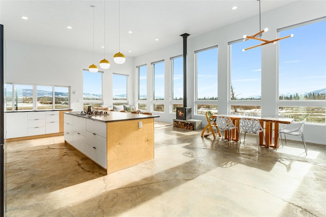 kitchen featuring concrete flooring, a wood stove, white cabinets, modern cabinets, and decorative light fixtures