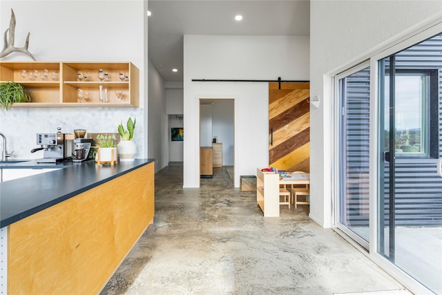 kitchen featuring a barn door, a sink, open shelves, dark countertops, and finished concrete floors