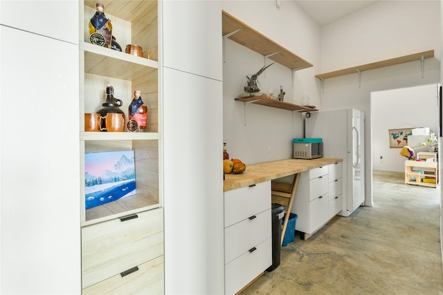 kitchen with white cabinets, modern cabinets, freestanding refrigerator, concrete floors, and open shelves