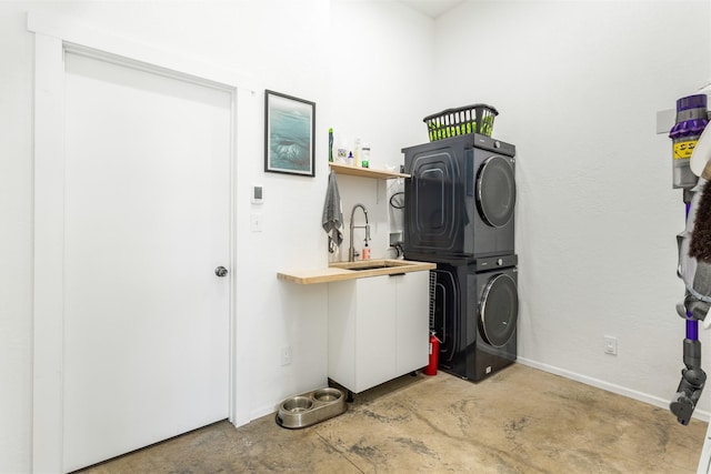 clothes washing area with a sink, laundry area, baseboards, and stacked washer / dryer