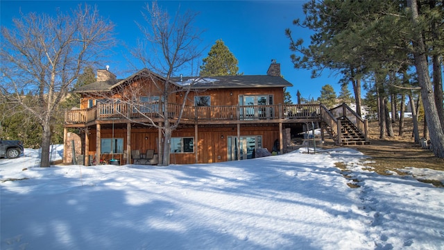 snow covered property featuring a deck, stairway, and a chimney