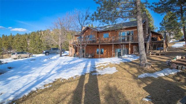 snow covered back of property with stairway and a wooden deck