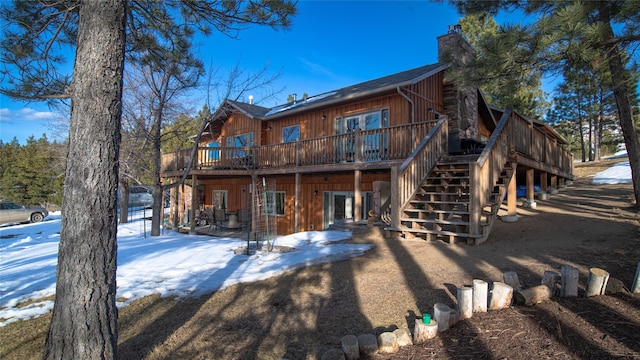 snow covered back of property with a chimney, stairway, a deck, and a patio