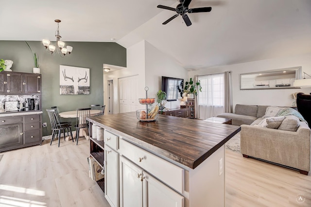 kitchen with lofted ceiling, butcher block countertops, open floor plan, light wood-type flooring, and ceiling fan with notable chandelier