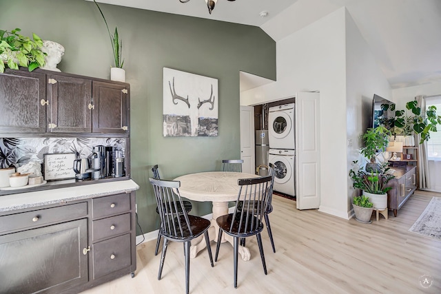 dining area with high vaulted ceiling, light wood-type flooring, baseboards, and stacked washing maching and dryer