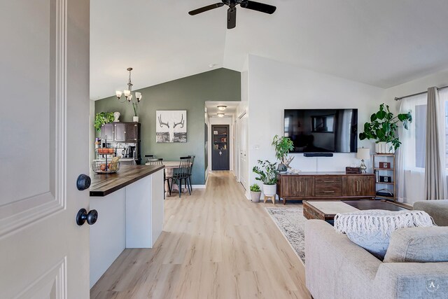 living area featuring light wood-type flooring, vaulted ceiling, baseboards, and ceiling fan with notable chandelier