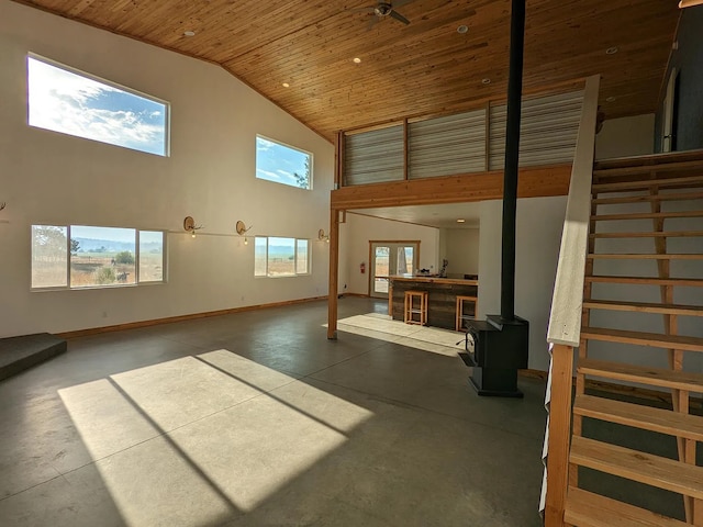 living area featuring baseboards, wooden ceiling, a wood stove, concrete flooring, and high vaulted ceiling