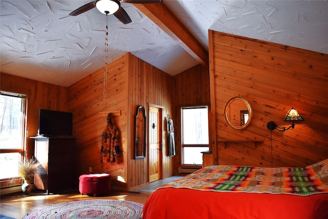 bedroom with multiple windows, wood walls, lofted ceiling with beams, and wood finished floors