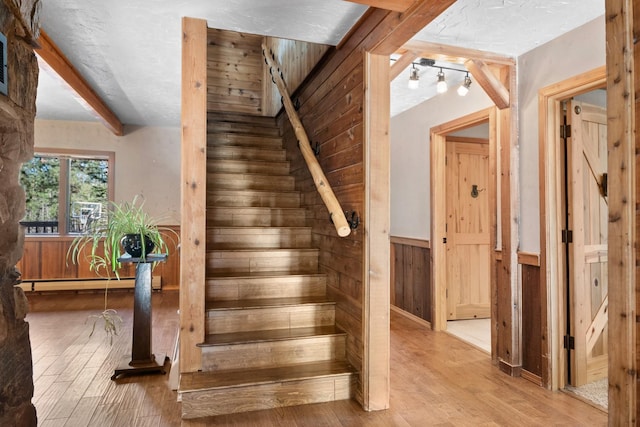 437 Tie Chute Ln, Florence, MT 59833 - staircase featuring hardwood / wood-style floors, wooden walls, baseboard heating, wainscoting, and a textured ceiling