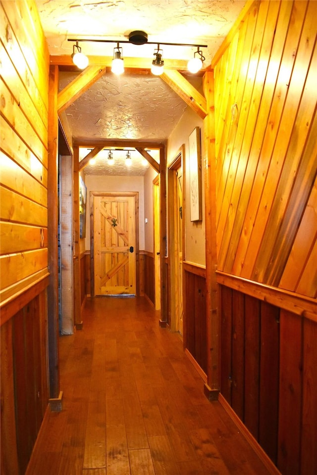 corridor with track lighting, wood-type flooring, wooden walls, and a textured ceiling