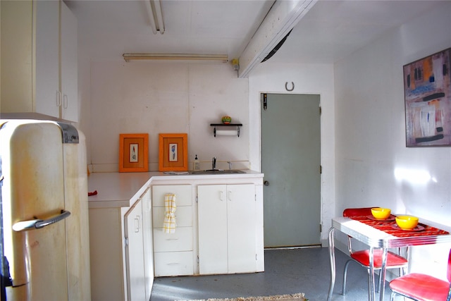 kitchen with a sink, white cabinetry, light countertops, open shelves, and finished concrete floors