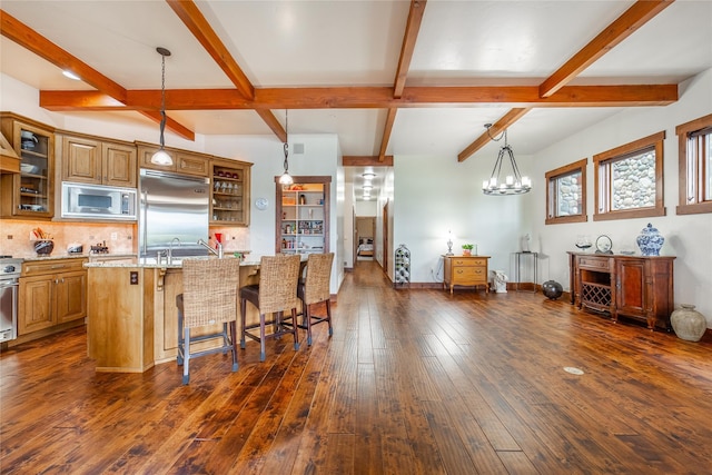 kitchen featuring light stone counters, a breakfast bar area, dark wood-type flooring, a kitchen island with sink, and built in appliances