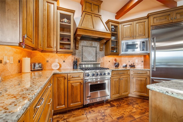 kitchen with built in appliances, light stone countertops, dark wood-style flooring, brown cabinets, and custom range hood