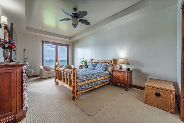 carpeted bedroom featuring a raised ceiling, ceiling fan, and baseboards