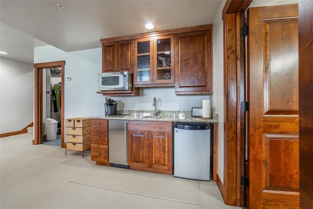 kitchen featuring light colored carpet, a sink, light stone countertops, stainless steel microwave, and glass insert cabinets