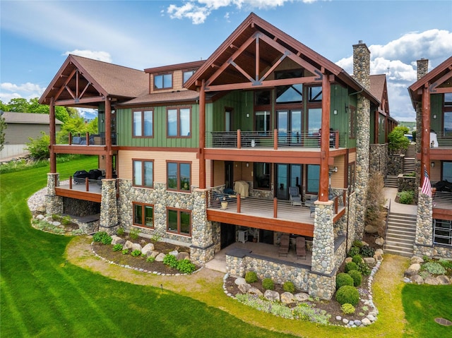 back of house featuring a patio, a balcony, stairs, a yard, and stone siding